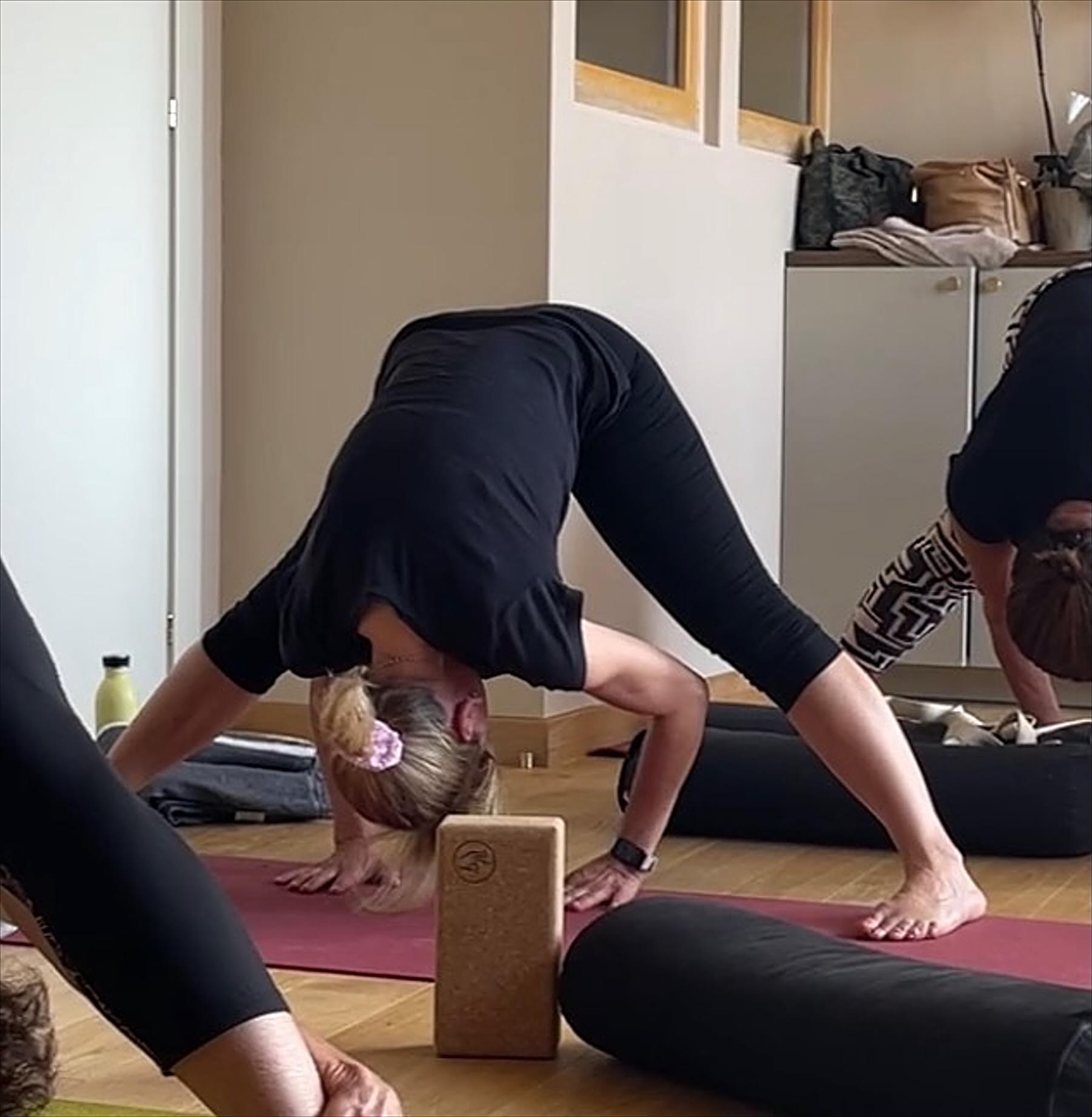 Pendant un cours en petit groupe : une élève en flexion avant jambes écartées, la tête posée sur une brique